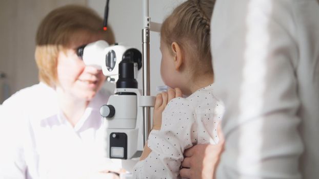 Little girl and her mommy in ophthalmology - optometrist checking little child's vision, close up