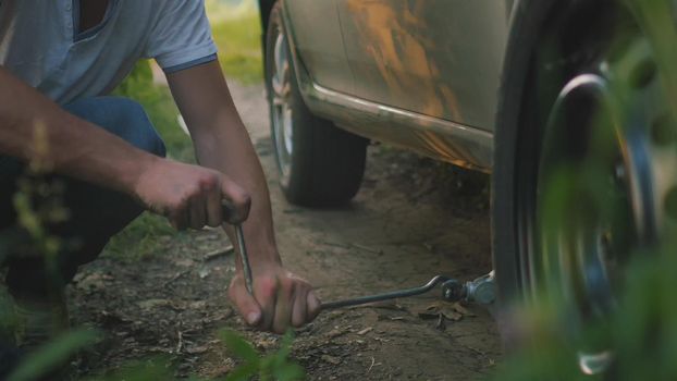 Close up view of man changes broken wheel of a car in the woods, telephoto