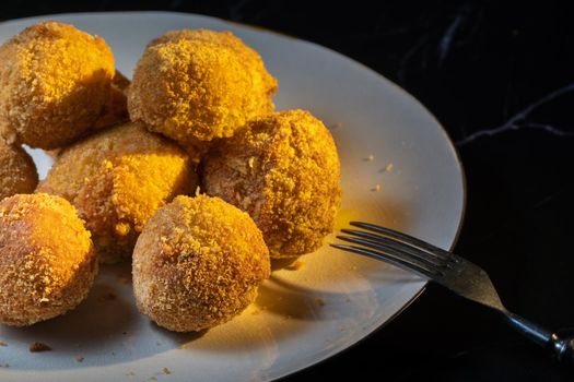 cheese balls with garlic and dill inside for a snack in a white plate on a black background.