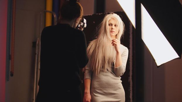 Professional photo session - blonde female model standing near studio flash - photographer's working, telephoto