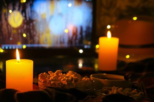 Movie on laptop at night in bedroom lit with candles. Pop corn. Autumn atmosphere at home. Cozy hygge style