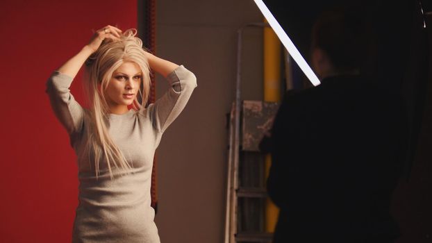 Cute caucasian blonde female model posing for photographer - fashion backstage, telephoto