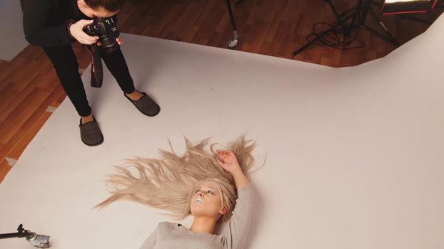 Attractive blonde model girl lying in photo studio - posing for photographer, white background