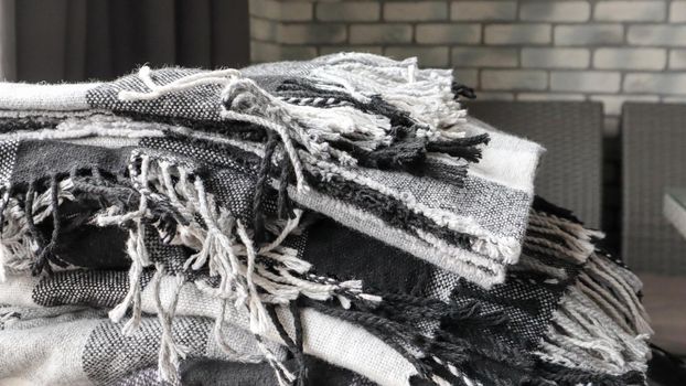 heap of knitted plaids on a gray background. Warm and cozy woolen decor for home and cafe. Gray wall background. Copy space. Gray checkered blanket. Warm and cozy home, selected focus.