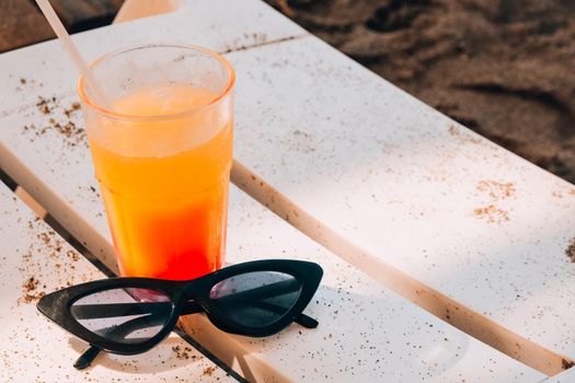 Fresh cold mango smoothie cocktail on tropical beach bright sand. Summer sea vacation and travel concept. Glass of fruit cocktail and sunglasses. Summertime vacation