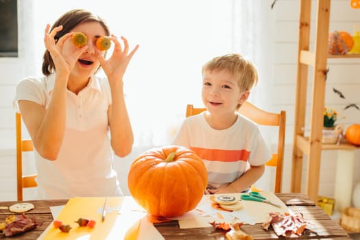 Happy Halloween. Young woman with her little son are preparing to Halloween on kitchen. Mother with son are having fun with pumpkins. Happy Halloween concept .