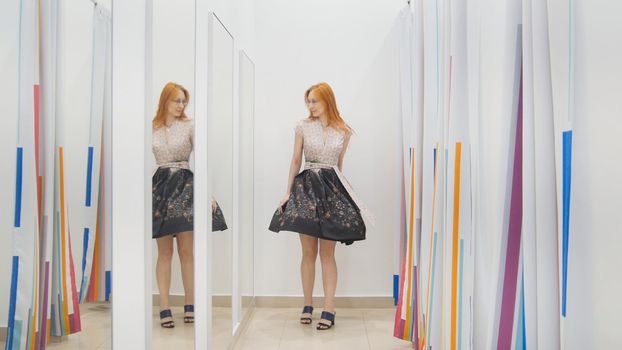 Young woman trying dress near mirror in fitting room - shopping concept, horizontal