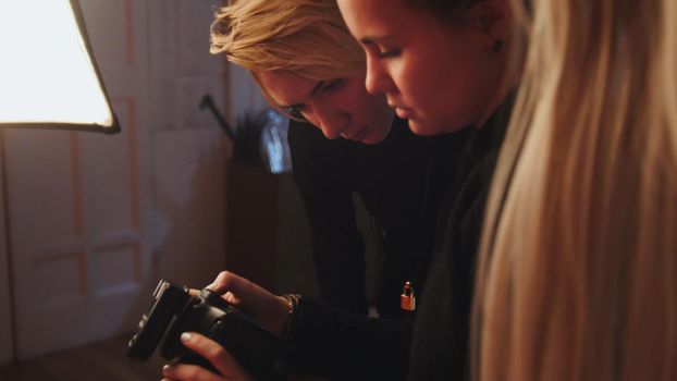 Blonde girl model and photographer in photo studio watching photos in camera, fashion backstage, horizontal