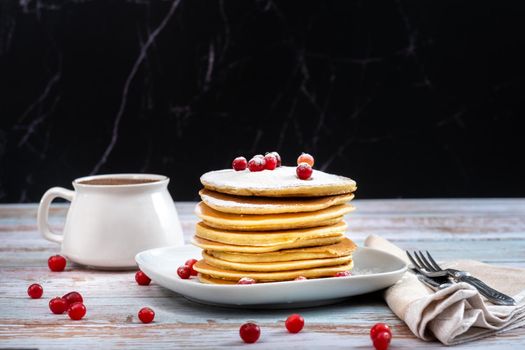 morning breakfast of pancakes with cranberries and powdered sugar and a cup of coffee on a wooden table.