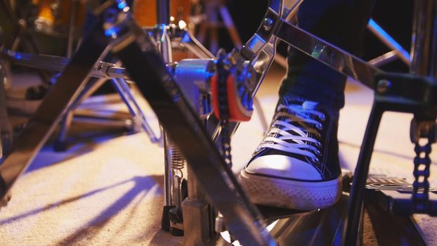 Drummer's foot in sneakers moving drum bass pedal, close up