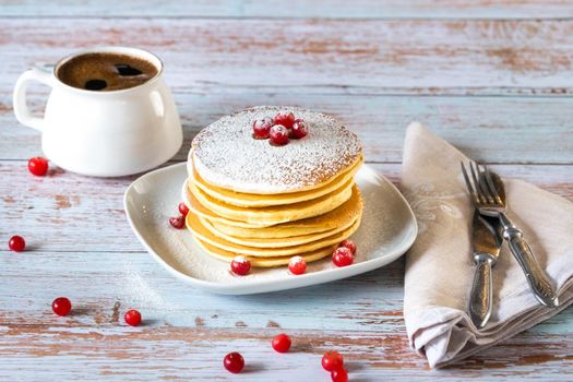 morning breakfast of pancakes with cranberries and powdered sugar and a cup of coffee on a wooden table.