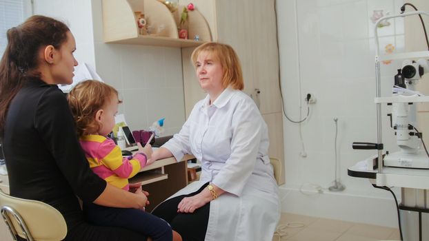 Optometrist checks child's eyesight - mother and child have consultation in ophthalmologist room, horizontal