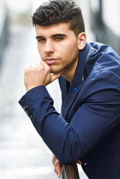 Good looking young man with blue eyes in the street. Model of fashion in urban background wearing white t-shir and blue jacket