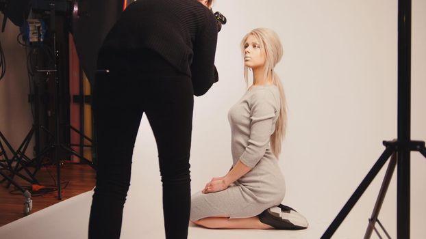 Workshop backstage - Blonde handsome girl posing for photographer - model sits at knees, white background