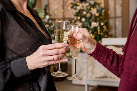 Close up of couple hands holding glasses of champagne over Christmas tree with lights