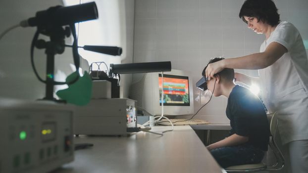 Ophthalmology doctor checks the boy's vision with the help of stereovideo virtual reality glasses, wide angle