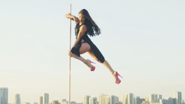 Fit attractive girl dancing on the portable pole at summer day over the skyline, slow-motion, near river, telephoto