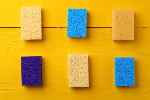 Cleaning sponges on yellow wooden background flat lay top view