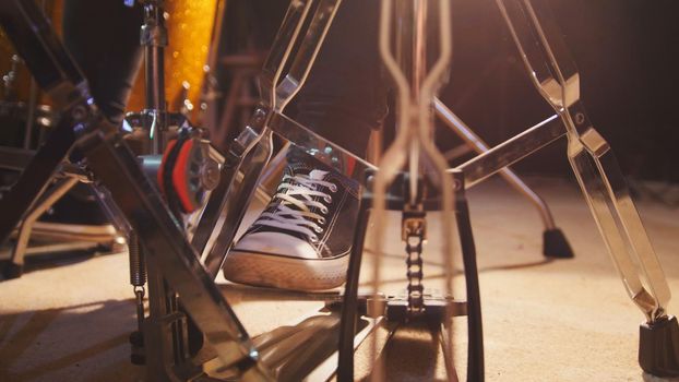 Drummer's foot in sneakers moving drum bass pedal, close up