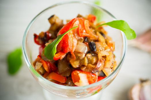 fried eggplants with peppers, tomatoes, onions and garlic in a glass bowl on a light wooden table