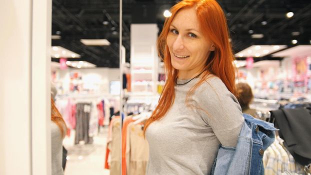Young attractive woman is choosing a jeans jacket in women's clothing store, close up