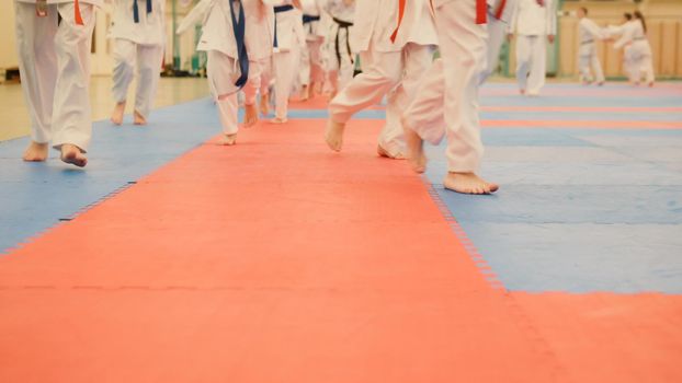 Karate training - young sportsmen in kimono runs on tatami in the gym, telephoto view