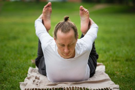 A man - yoga instructor performs flexibility exercises in park, telephoto shot