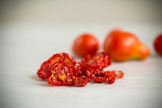 a handful of dried tomatoes and fresh tomatoes on a light table