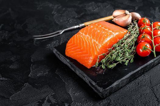 Protein vegetarian diet - raw salmon fillet steak with herbs and tomato. Black background. Top view. Copy space.