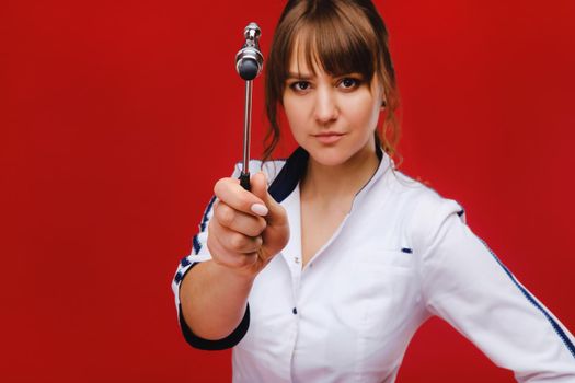 The doctor is holding a neurological hammer on a red background. The neurologist checks the patient's reflexes with a hammer. Diagnostics, healthcare, and medical care.