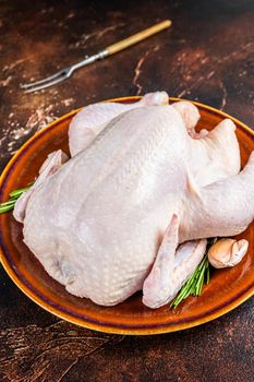 Chicken, raw poultry in a rustic plate with rosemary. Dark background. Top view.