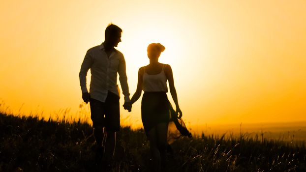 loving couple - brave young man and beautiful girl at sunset silhouette, over the sun, telephoto