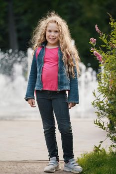 Little blonde smiling child wearing jeans jacket in park, outdoor portrait