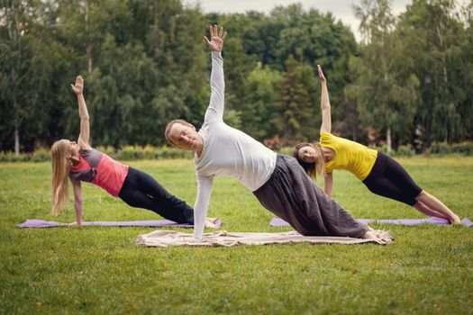 Training in park - instructor shows flexibility exercise for group of girls in park, early morning