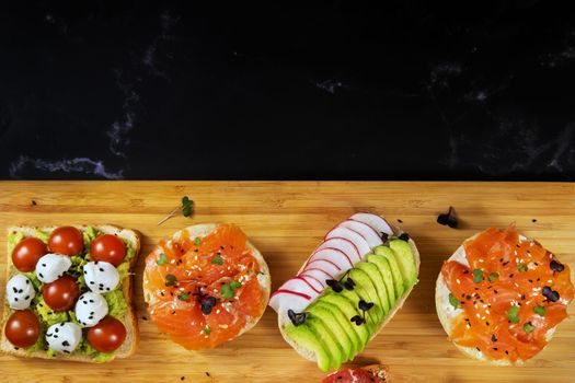 Assorted sandwiches with fish, cheese, meat and vegetables lying on the board.