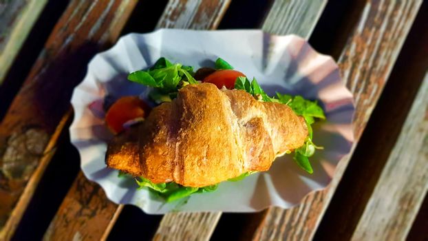 Croissant with avocado, tomato and herbs outdoors. Street vegetarian food.