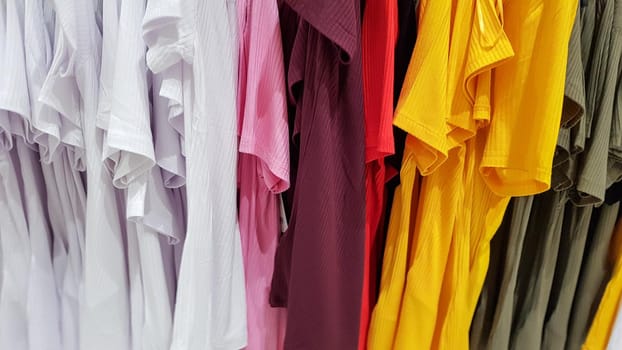 Colors of rainbow. Variety of casual shirts, t-shirts on hangers in a store. Cloth cotton of various bright colors close-up. Textile background.