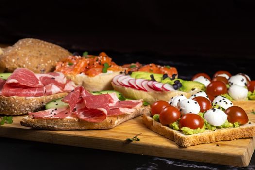 Assorted sandwiches with fish, cheese, meat and vegetables lying on the board.