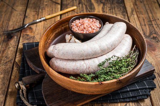 Raw Munich traditional white sausages in a wooden plate with herbs. wooden background. Top view.