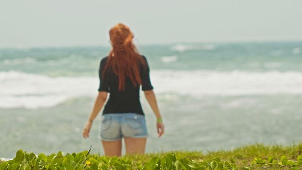 Young woman with long red hair on caribbean beach, Dominican Republic, rear view, telephoto