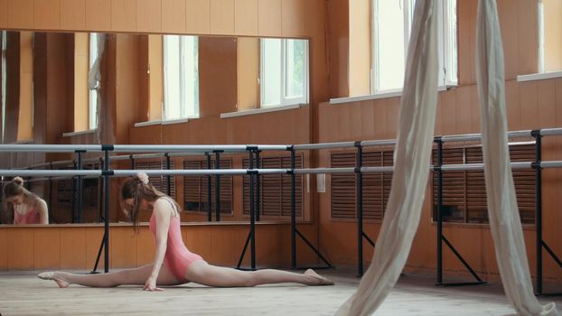 Beautiful gymnast does the splits in a room with ballet lathe and mirrors, circus artist
