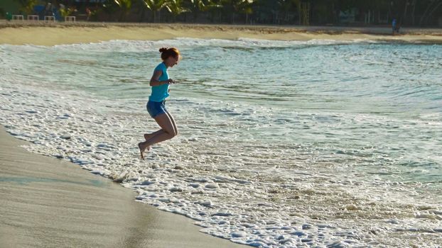 Young woman with long red hair play with waves running, feeling the sea, seascape beach of Dominican Republic, wide angle, Caribbean sea