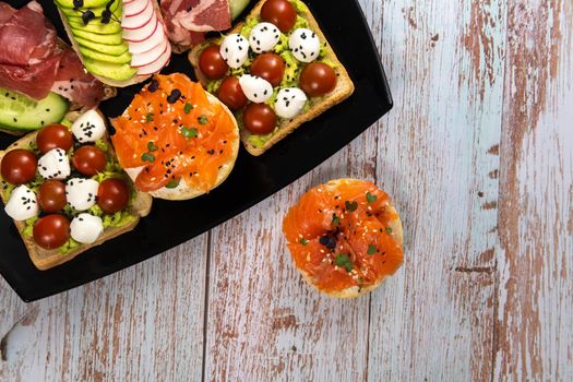 Assorted sandwiches with fish, cheese, meat and vegetables on a black plate.