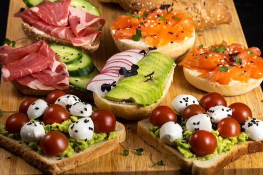 Assorted sandwiches with fish, cheese, meat and vegetables lying on the board.