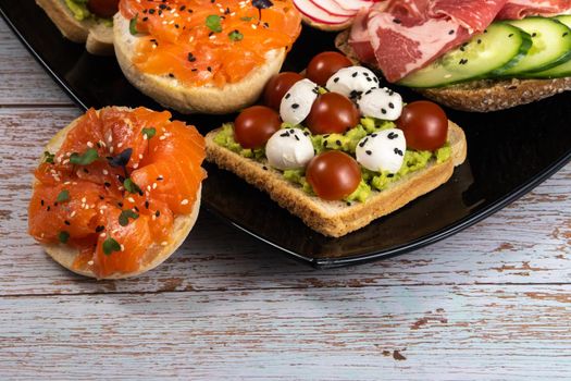 Assorted sandwiches with fish, cheese, meat and vegetables on a black plate.