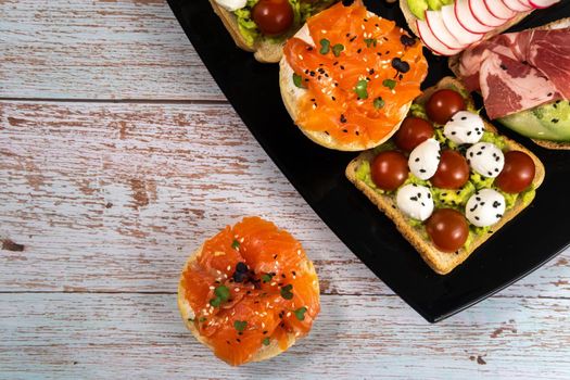 Assorted sandwiches with fish, cheese, meat and vegetables on a black plate.