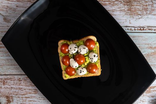 A cheese and tomato sandwich sits in a black plate on a wooden background.