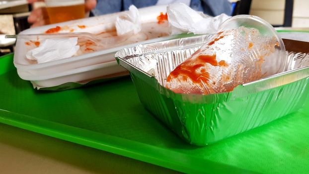 Leftover food, dirty plastic dishes on a green tray on a table in an outdoor cafe.