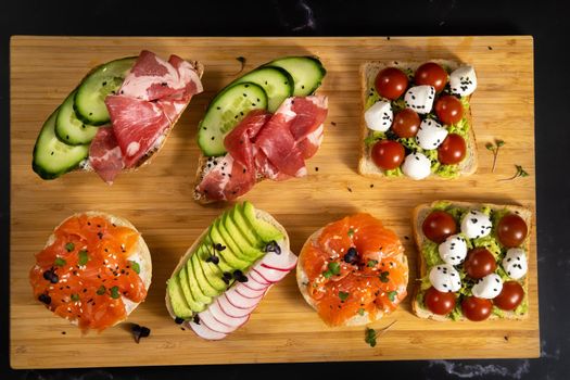 Assorted sandwiches with fish, cheese, meat and vegetables lying on the board.