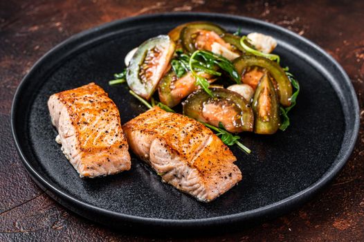 Grilled Salmon Fillet Steaks with arugula and tomato salad on a plate. Dark background. Top view.